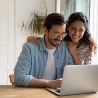 Happy couple use modern laptop at home together Happy Caucasian young couple look at laptop screen browse surf wireless internet on gadget. Smiling millennial man and woman shopping paying on internet on computer at home. Technology concept.